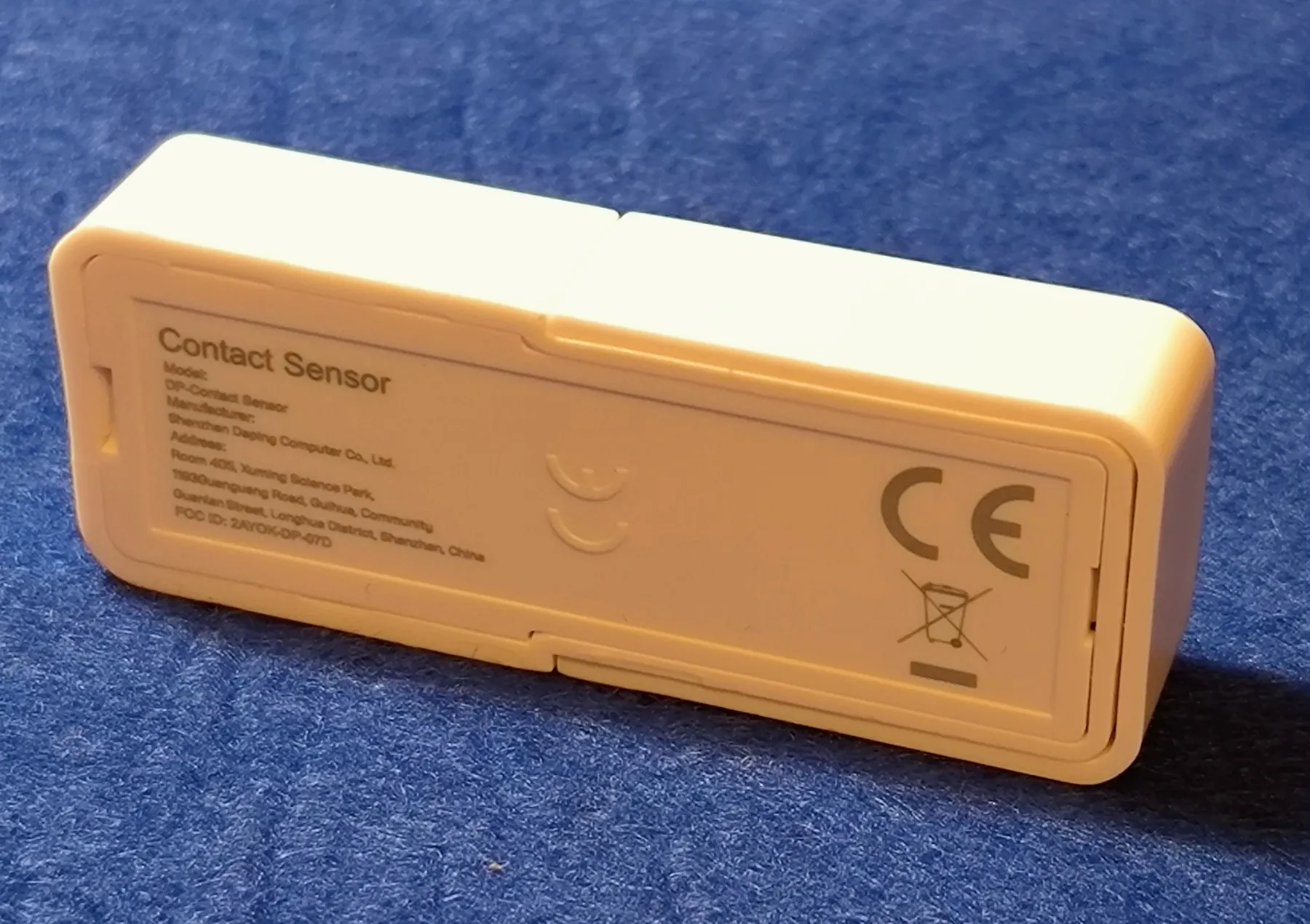 The contact sensor in its closed white case, sitting on a blue cloth